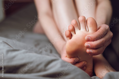 Tired female feeling discomfort rubbing her sore and painful foot and toes, during exercise sitting on bed at home. Woman foot massage to relieve pain from ache. Tense sore sprained muscle © Yura Yarema