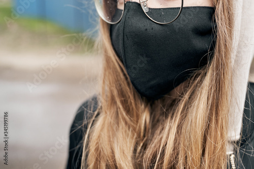 Girl in a mask with glasses stands on the street during a light rain.