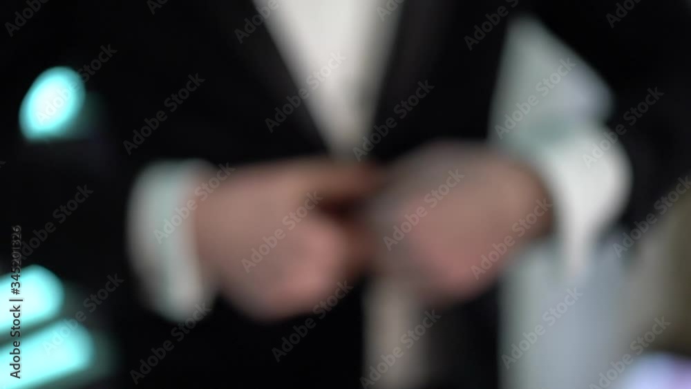 A male silhouette in a black suit in out of focus fastens a button on the jacket, the camera zooms in and improves focus, a male hand goes down hold the edge of the jacket A male silhouette in a black suit in out of focus fastens a button on the jacket, the camera zooms in and improves focus, a male hand goes down hold the edge of the jacket