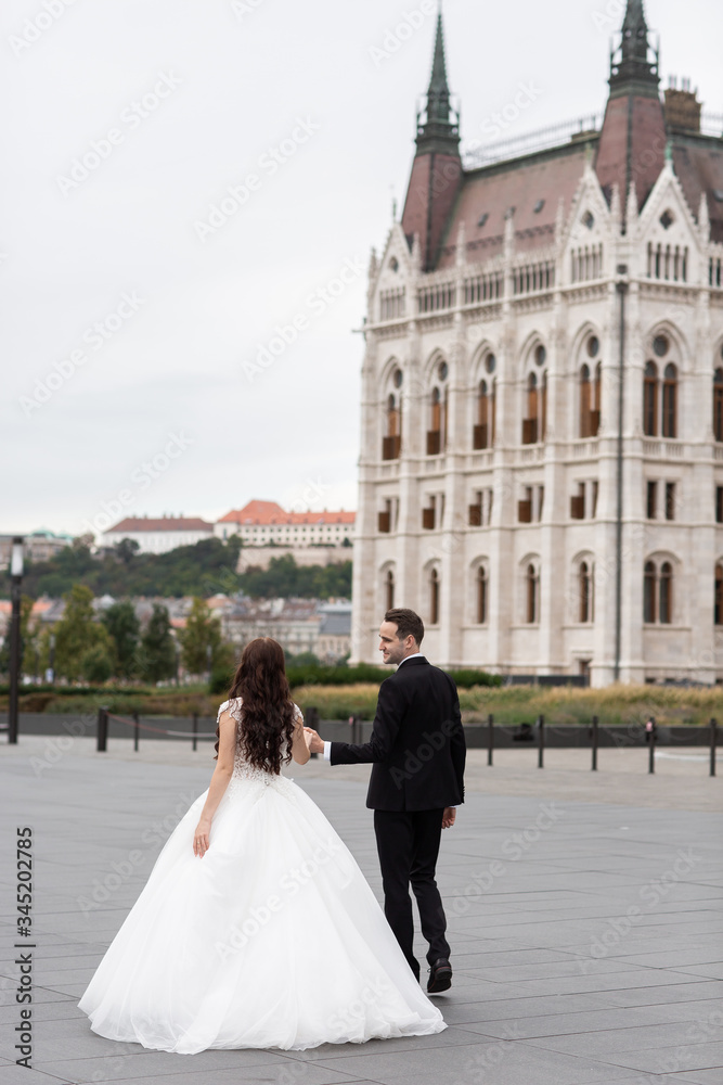 Bride and groom dancing in the old town street. Wedding couple walks in Budapest near Parliament House. Caucasian happy romantic young couple celebrating their marriage. Wedding and love concept.