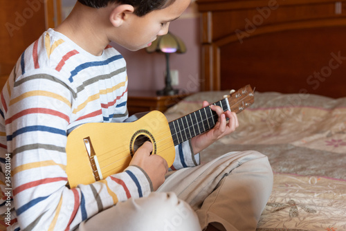 Side view of a little boy playing timple at home. photo