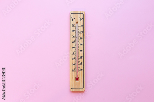 A classic wooden thermometer on pink background shows a high temperature of 20 degrees centigrade and 70 degrees fahrenheit photo
