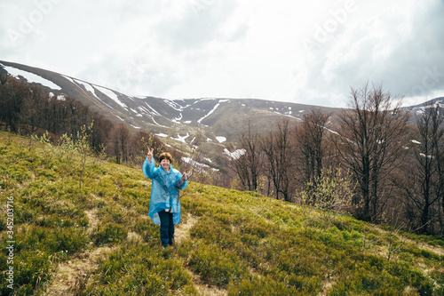 Happy smiling traveller senior beautiful woman in blue rain jacket and jeans in mountains surrounded by forest, enjoying silence and harmony of nature © Iryna Budanova