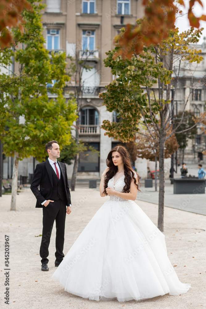 Fototapeta premium Bride and groom dancing in the old town street. Wedding couple walks in Budapest near Parliament House. Caucasian happy romantic young couple celebrating their marriage. Wedding and love concept.