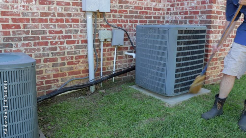 Person cleans area around an air conditioner units next to brick home