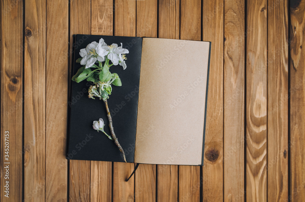 Black and beige notebook with a sprig of a blossoming apple tree. The concept of creativity, ideas, floristry and writing. Wooden background, vintage paper, mock up. Black and beige notebook with a sprig of a blossoming apple tree. The concept of creativity, ideas, floristry and writing. Wooden background, vintage paper, mock up.