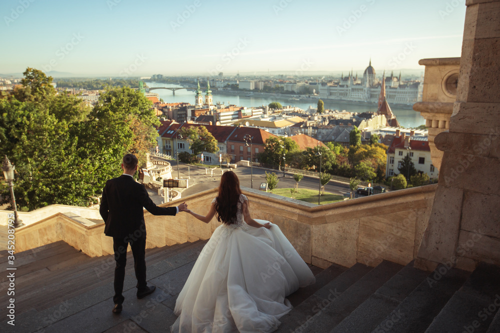 Bride and groom hugging in the old town street. Wedding couple walking on the Fisherman's Bastion, Budapest, Hungary. Happy romantic young couple celebrating their marriage. Wedding and love concept.