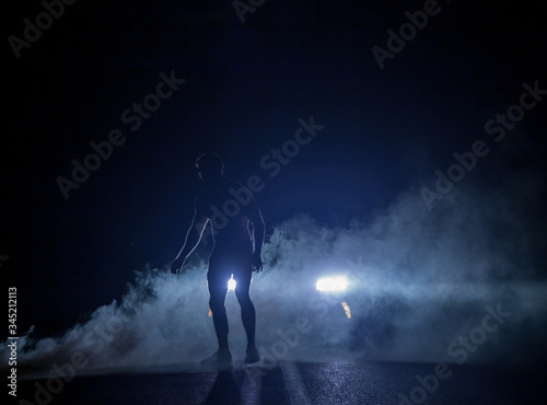 Mysterious figure in front of smoky car headlights