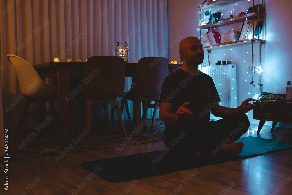 Young man doing yoga for peace in the dark in his house