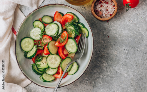 Healthy vegetable salad of fresh tomato, cucumber, dill and spices and oil in bowl on light gray background. Diet concept.