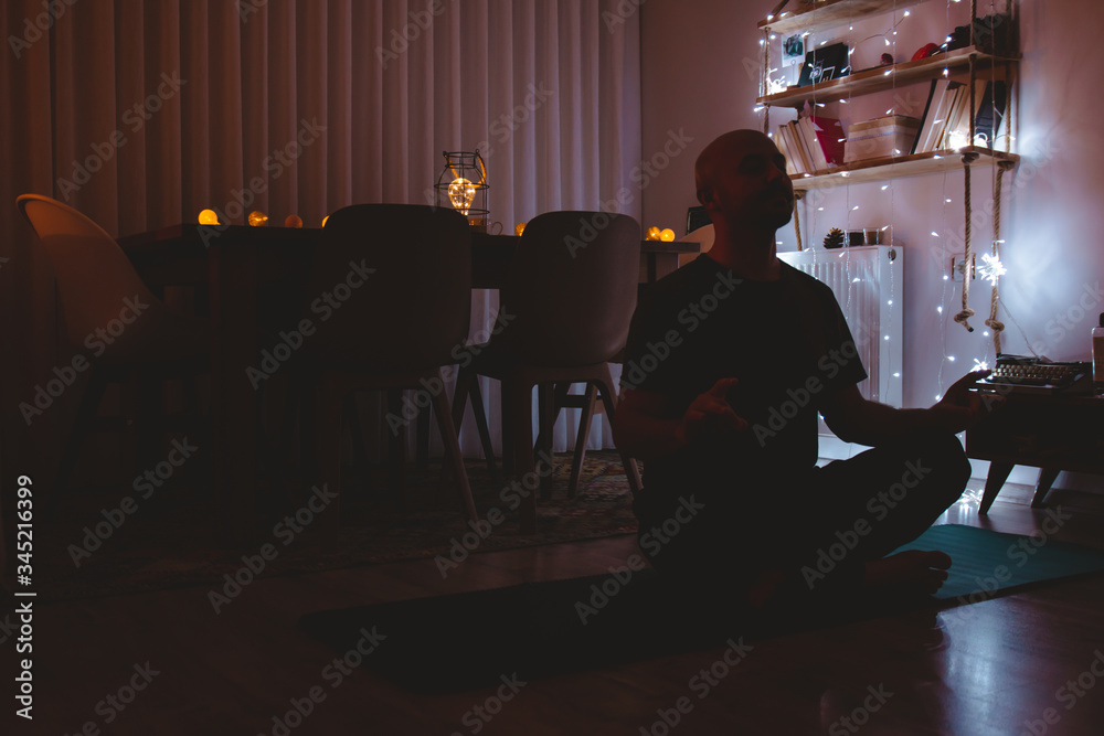 Young man doing yoga for peace in the dark in his house Young man doing yoga for peace in the dark in his house