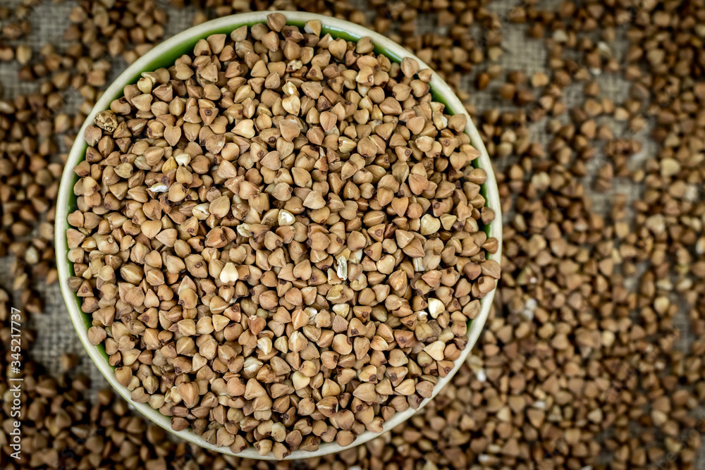 Buckwheat is poured in a round bowl (plate), close-up top view, around defocused buckwheat scattered around the table Buckwheat is poured in a round bowl (plate), close-up top view, around defocused buckwheat scattered around the table