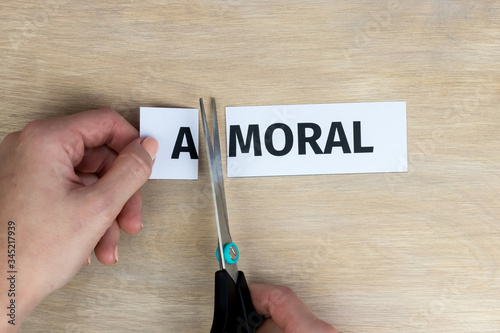 Woman cuts by scissors word "amoral", written on paper, so that word "moral" is obtained.