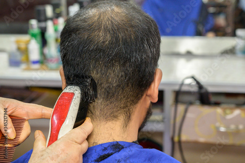 Rear view of Asian man getting haircut by hairdresser at the barbershop. Haircut refers to the styling of hair, usually on the human scalp.