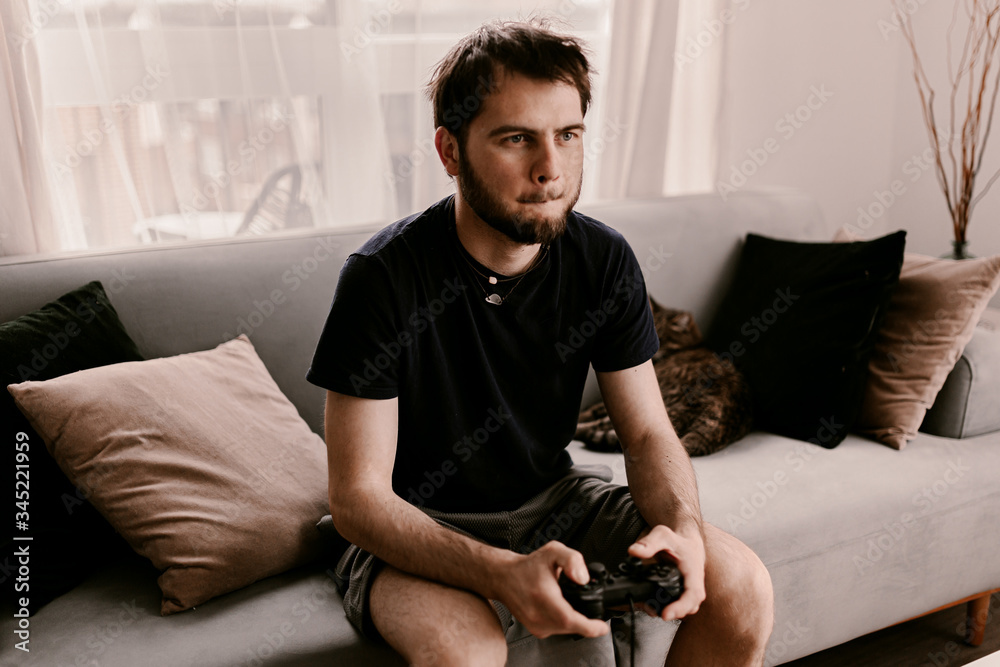Hipster man plays video games on a couch. Relaxing time. Fun weekend. Concentrated on a video game. Winning the game, gambling. Multiplayer game. Online gaming. Streaming video game. Soccer, racing