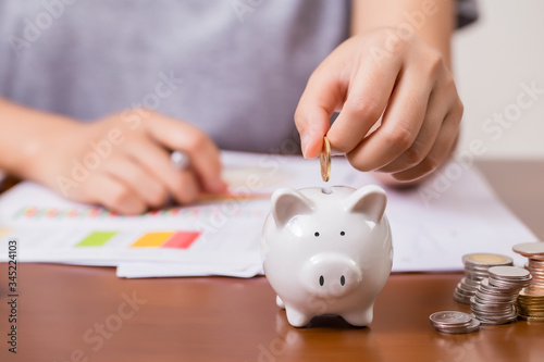 Female hand putting money into piggy bank for saving money.