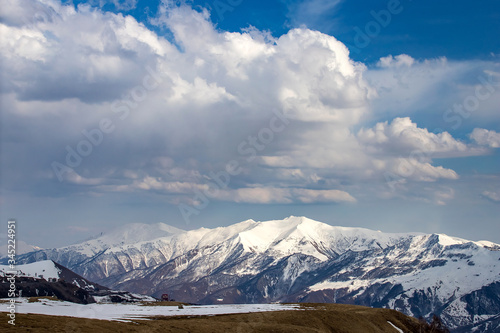 Panorama of the Caucasus mountains with clouds above them in the spring before sunset