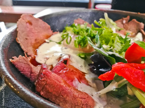 Premium Japanese beef Wagyu thin grilled and sliced topping with white Italian dressing sauce and salad in a bowl