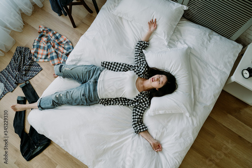 фотографія top view of taiwanese woman lying in a sprawl on bed with her clothes scattered on floor