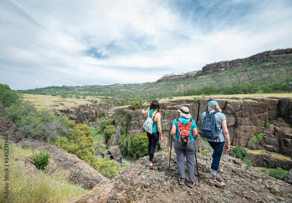 Three women hikers trekkers wearing backpacks survey vast landscape of bluffs and canyons