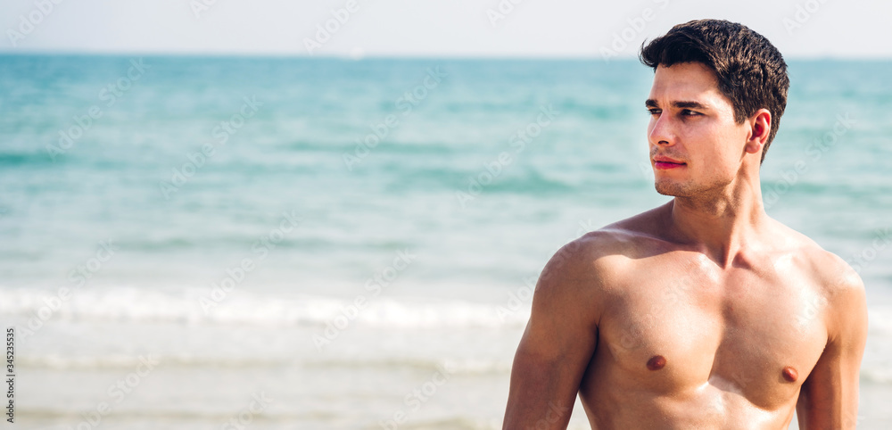 Portrait of smiling happy handsome sexy man showing muscular fit body enjoying and relax standing on the tropical beach.Summer vacations and travel