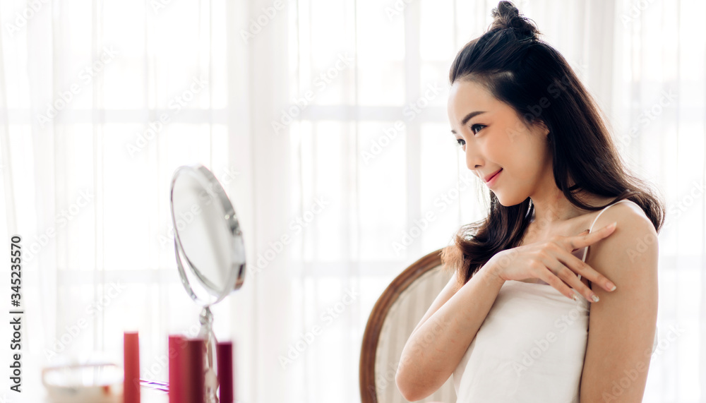 Smiling of young beautiful pretty asian woman clean fresh healthy white skin looking at mirror.girl touching on her face with hand and applying cream at home.spa and beauty concept Smiling of young beautiful pretty asian woman clean fresh healthy white skin looking at mirror.girl touching on her face with hand and applying cream at home.spa and beauty concept