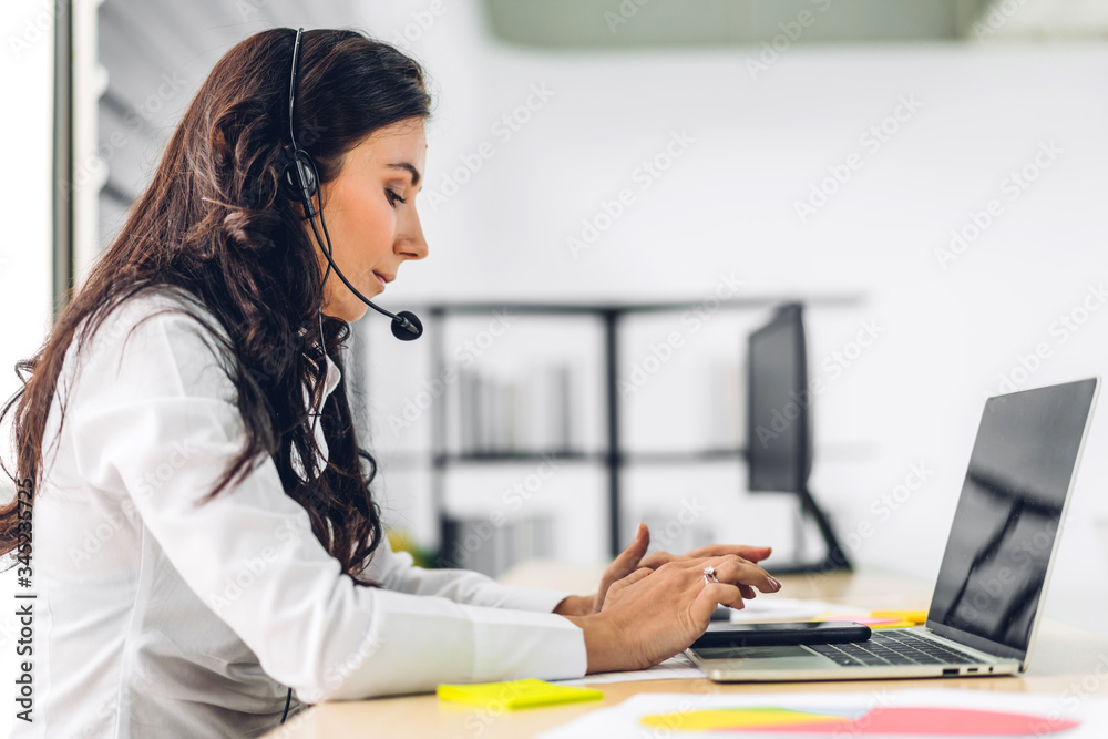 Beautiful happy call center smiling businesswoman operator customer support consult phone services agen working with wireless headset microphone and computer at call center office Beautiful happy call center smiling businesswoman operator customer support consult phone services agen working with wireless headset microphone and computer at call center office