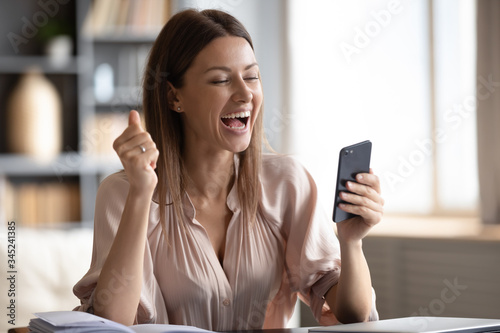 Excited happy woman looking at phone screen, celebrating online win, overjoyed young female screaming with joy, holding smartphone, reading good news in unexpected message or email photo