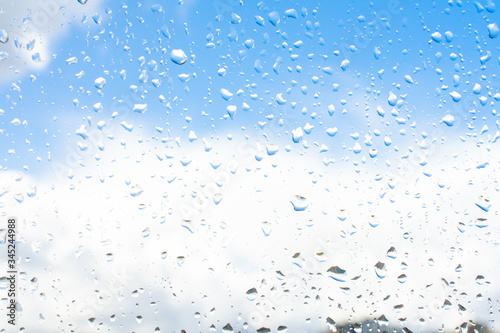 Raindrops on window glass against blue sky with white clouds