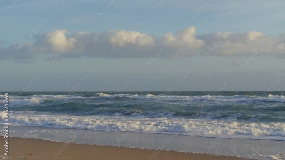 SLOW MOTION: Ocean shore on a bright sunny morning with raging waves. Strong waves are raging near the coastline of the sea, slow motion. Clouds over the ocean, oceanic background. Ocean shoreline. SLOW MOTION: Ocean shore on a bright sunny morning with raging waves. Strong waves are raging near the coastline of the sea, slow motion. Clouds over the ocean, oceanic background. Ocean shoreline.