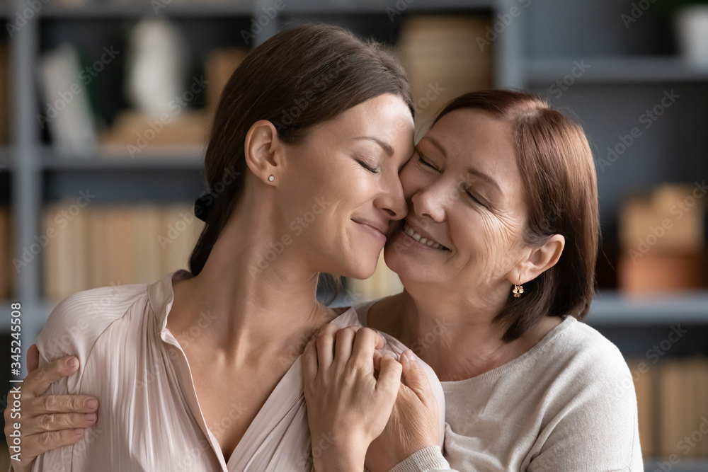 Happy adult daughter and mature mother hugging close up, expressing love and care, touching cheeks, smiling young woman enjoying tender moment with older middle aged mum, standing at home Happy adult daughter and mature mother hugging close up, expressing love and care, touching cheeks, smiling young woman enjoying tender moment with older middle aged mum, standing at home