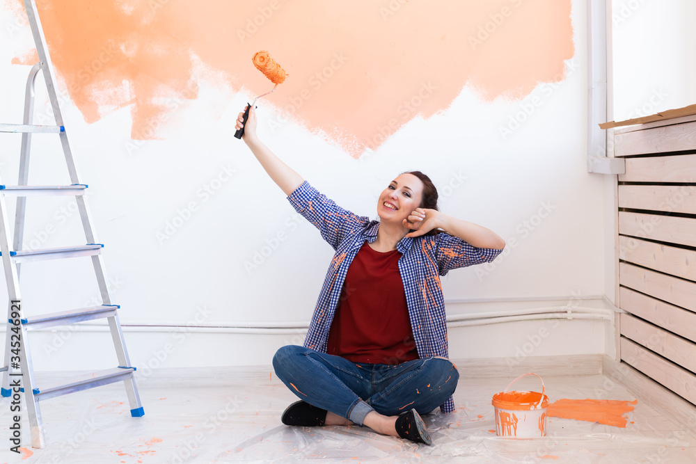 Beautiful female painting the wall with paint roller. Portrait of a young beautiful woman painting wall in her new apartment. Redecoration and renovation concept.