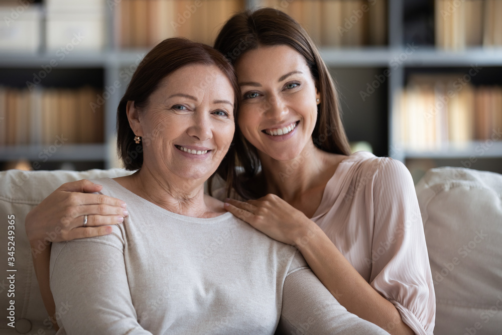 Head shot portrait smiling mature mother and daughter hugging, sitting
