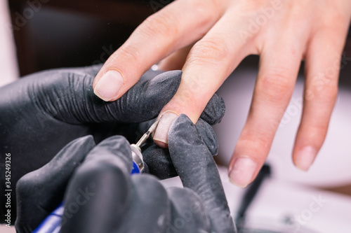 Woman use electric nail file drill in beauty salon. Nails manicure process in detail. Gel polish close-up concept.