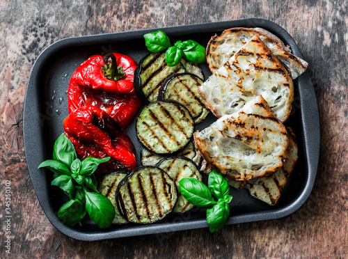 Summer grilled vegetables - eggplant, bell peppers and ciabatta bread, basil in baking sheet on wooden background, top view
