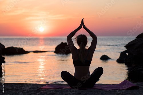 girl has a yoga practice on the beach among big stones. rocks in the sea. sunrise time © AlexR