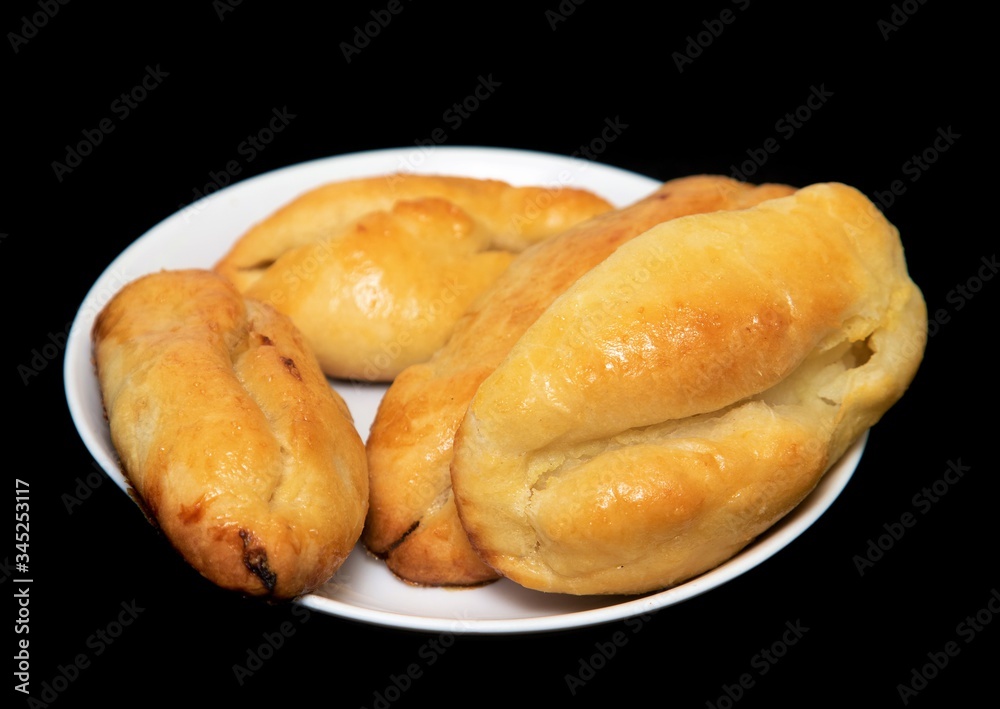 Baked pies lie on a white plate, on a black background. Baked pies lie on a white plate, on a black background.