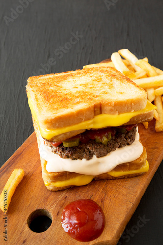 Fresh Grilled Cheese Burger with French Fries on a rustic wooden board on a black background, side view. Copy space.