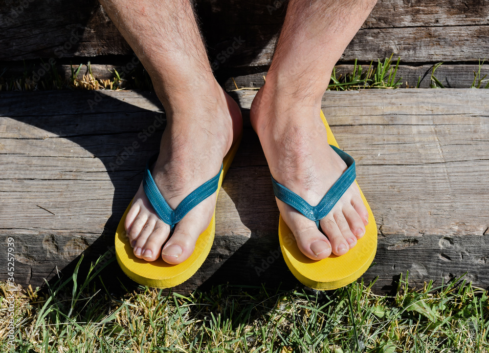 a couple of feet completely barefoot wearing two yellow and blue flip flops on a wooden step. The man is resting in the garden in a sunny day of summer. Horizontal photo . a couple of feet completely barefoot wearing two yellow and blue flip flops on a wooden step. The man is resting in the garden in a sunny day of summer. Horizontal photo .