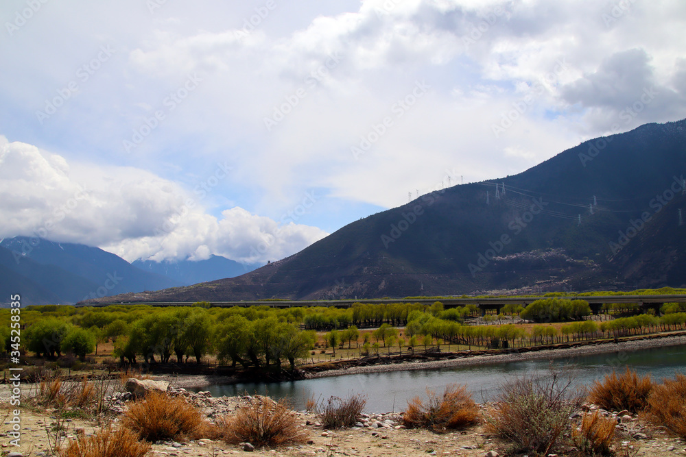 Blue sky and white clouds, distant mountains, green water, sandbars and trees by the river, like beautiful pictures