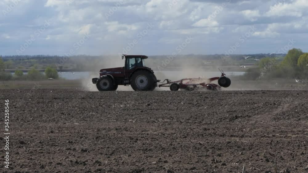 Farmer on Tractor Plowing Dusty Arid Soil. Farm Car Followed by Flock Birds. Tractor Cuts Furrows in Farm Field for Sowing. Agribusiness in Spring. Sowing Agricultural Crops Farmer on Tractor Plowing Dusty Arid Soil. Farm Car Followed by Flock Birds. Tractor Cuts Furrows in Farm Field for Sowing. Agribusiness in Spring. Sowing Agricultural Crops