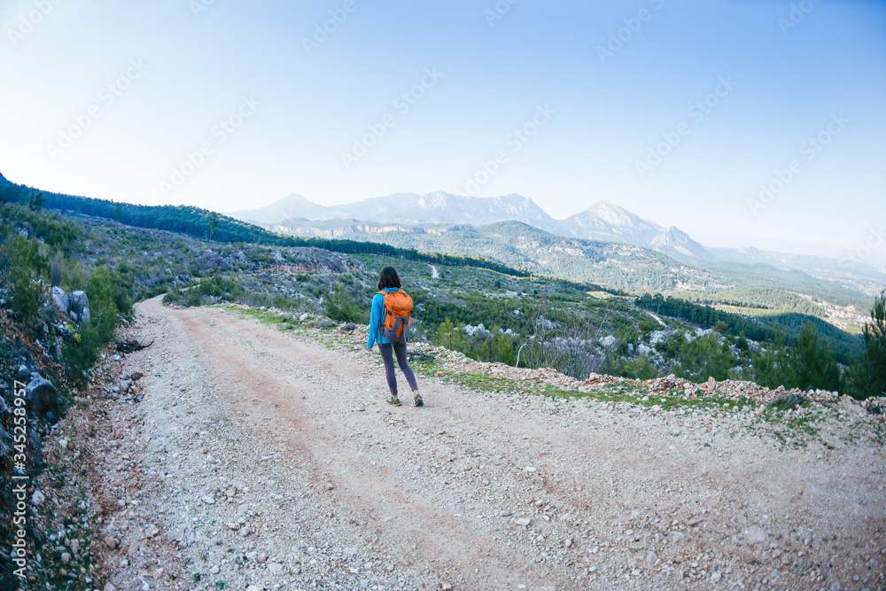 A woman with a backpack is walking along a mountain road.