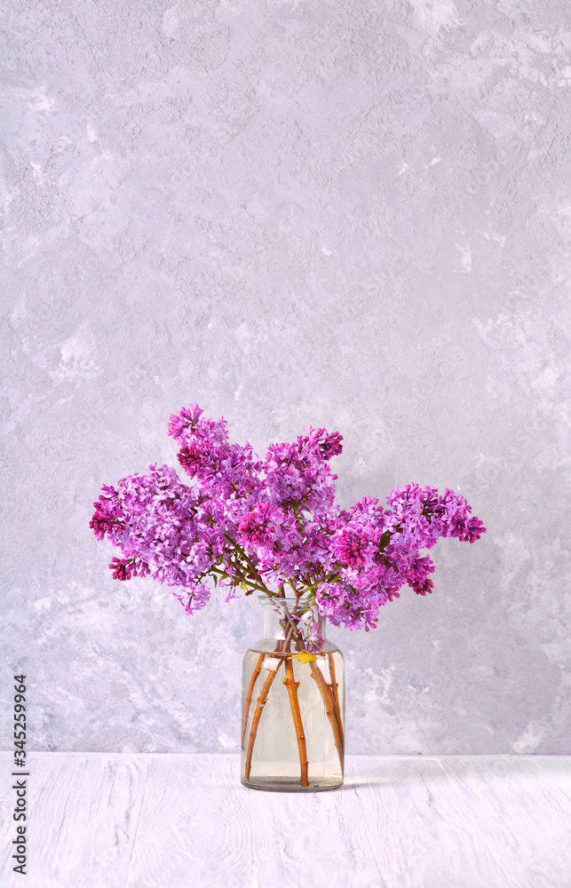 Obraz premium Beautiful blooming lilac branches in the glass jar on the table. Vertical.