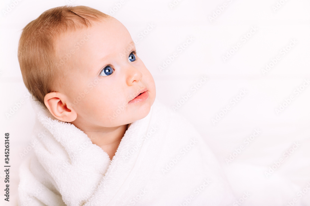A cute baby with blue eyes wrapped in a white towel looks away. Copy space. A cute baby with blue eyes wrapped in a white towel looks away. Copy space.