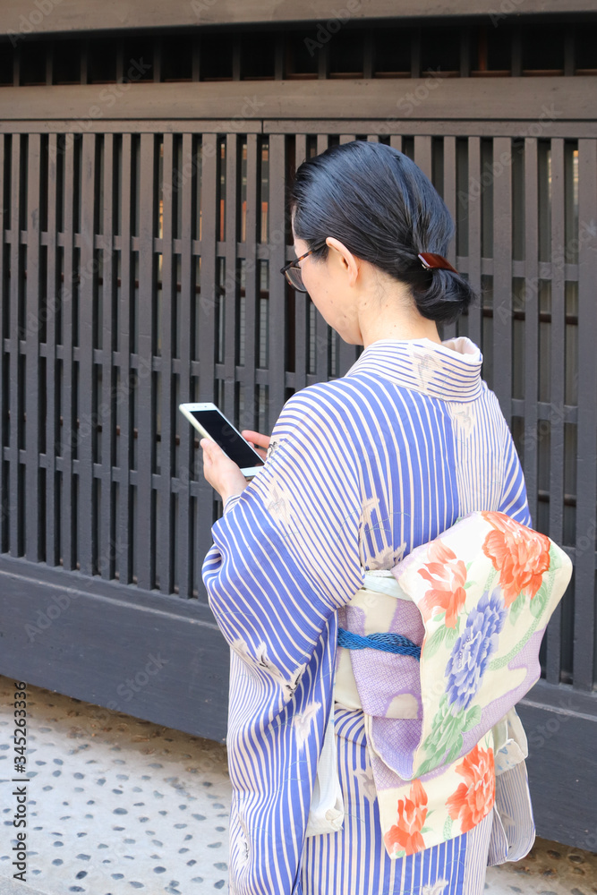 Japanese woman in kimono checking her smartphone by traditional building