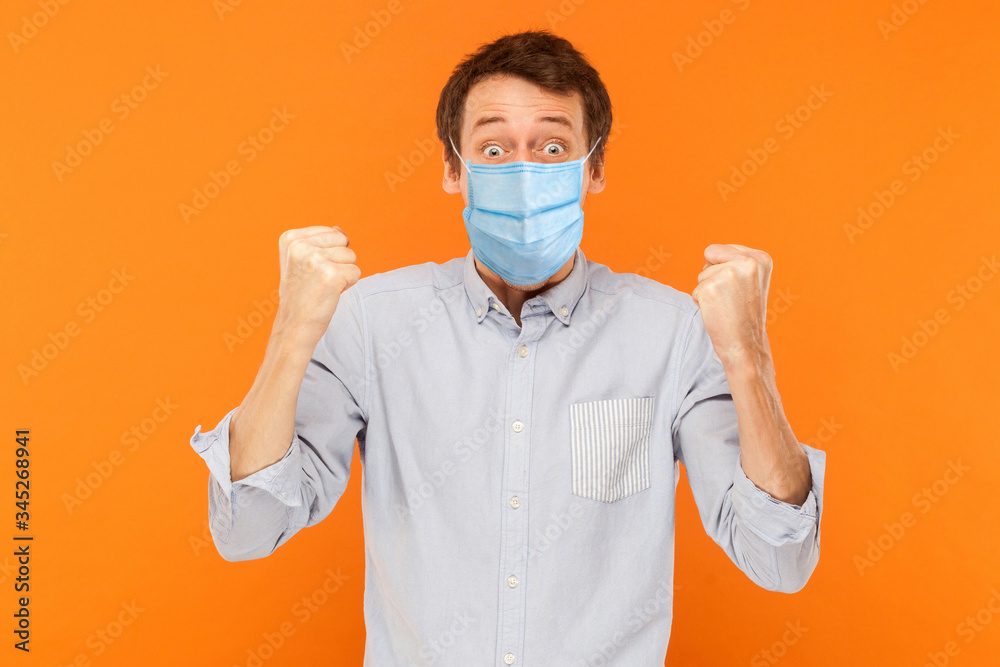 Yes. Portrait of surprised young worker man with surgical medical mask standing and celebrating his victory and looking at camera. indoor studio shot isolated on orange background. Yes. Portrait of surprised young worker man with surgical medical mask standing and celebrating his victory and looking at camera. indoor studio shot isolated on orange background.