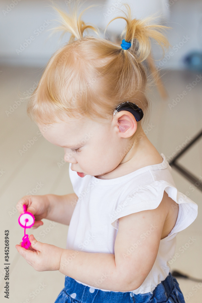Fototapeta premium Hearing aid in baby girl's ear. Toddler child wearing a hearing aid at home. Disabled child, disability and deafness concept.