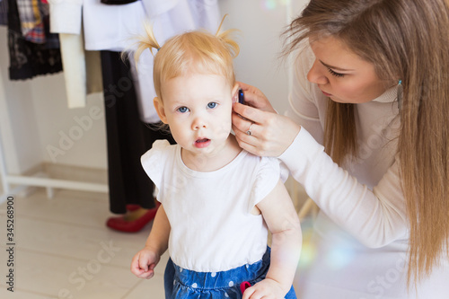 Hearing aid in baby girl's ear. Toddler child wearing a hearing aid at home. Disabled child, disability and deafness concept.