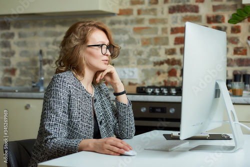 A woman in glasses works remotely on a desktop computer in her studio. A female boss listening to a report of employee at a video conference at home. A female professor preparing for an online lecture