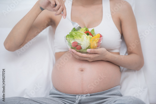 care about unborn child. pregnancy, healthy food and people concept, happy pregnant woman eating vegetable salad for breakfast sitting on bed at home. pregnancy and healthy organic nutrition.